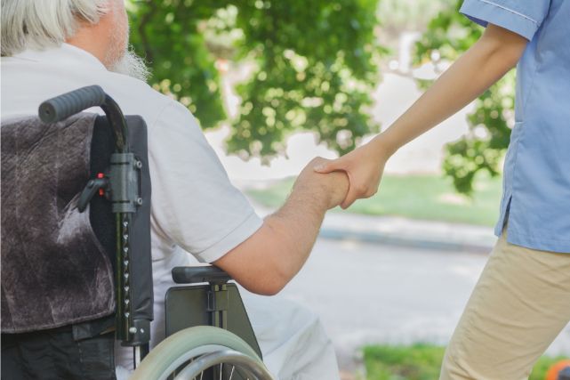 高齢の車椅子の男性と手を繋ぐ介護士